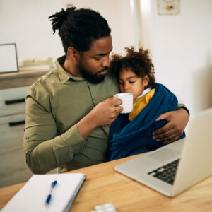 Caring black father giving a cup of tea to his sick small daughter at home.