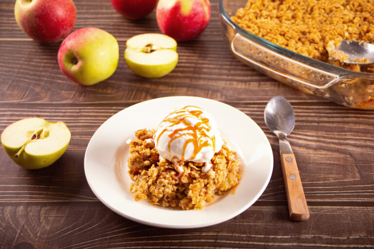 Homemade apple crumble crisp cake on white plate with autumn leaves on the wooden background.