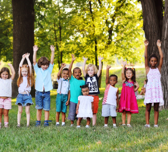 A group of children outside raising their arms excitedly