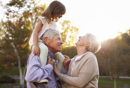 A smiling elderly couple with their grandchild on the grandpa's shoulders